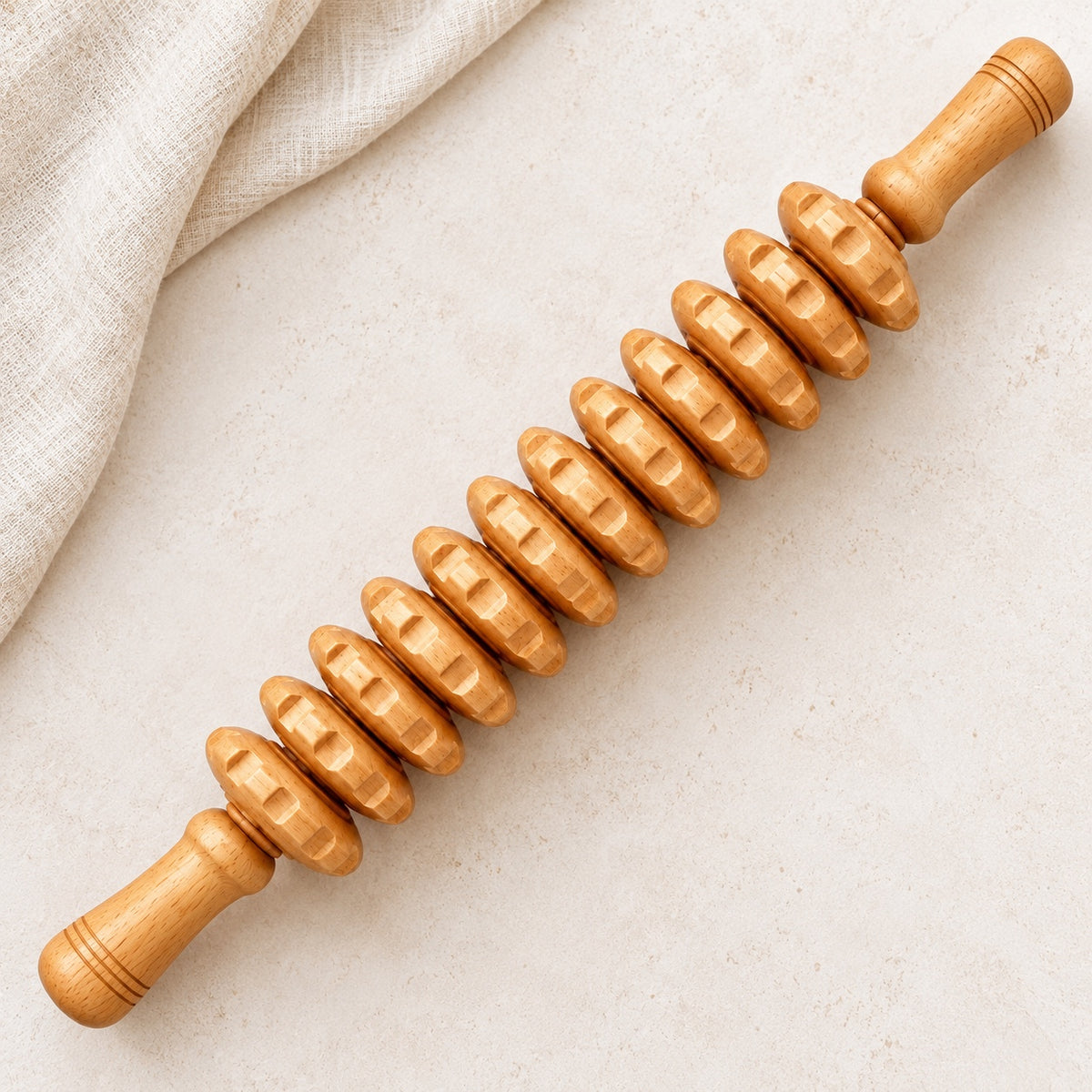 Rouleau de massage à disques en bois présenté sur un fond clair avec du lin.